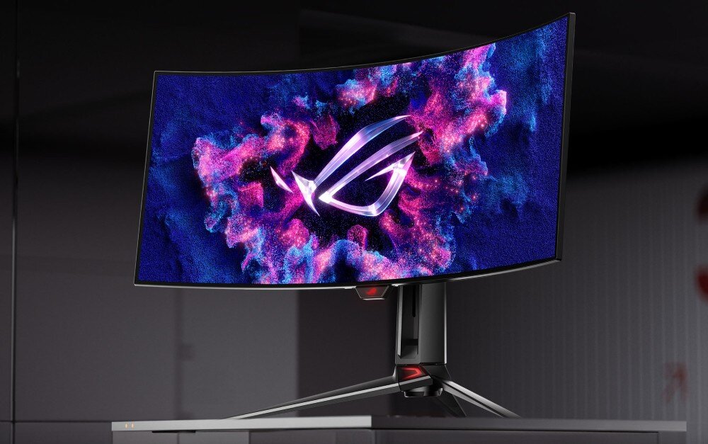 Monitor ASUS ROG Swift PG34WCDM Zakrzywiony monitor gamingowy z podświetlonym logo na ekranie, otoczonym efektownymi różowo-niebieskimi wzorami. Urządzenie stoi na biurku w ciemnym pomieszczeniu, opis