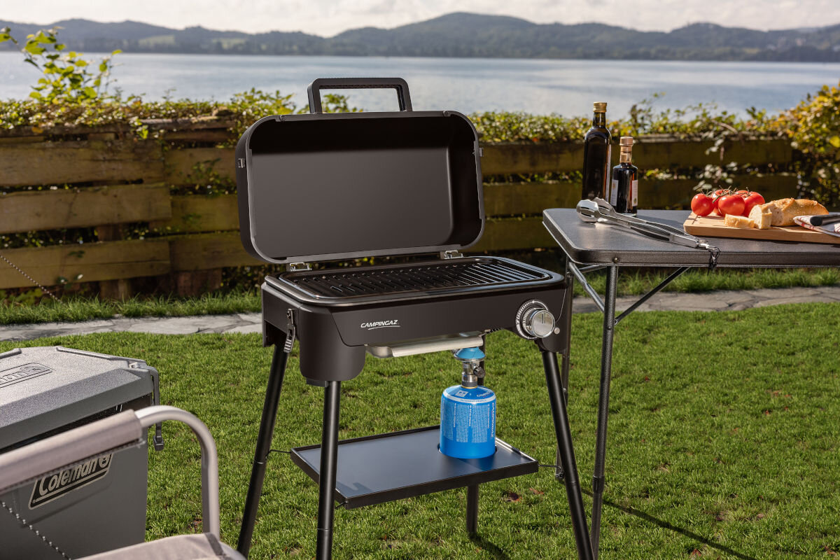 Grill gazowy CAMPINGAZ Tour and Grill 2.4 kW 47 x 25.5 cm, palnik, gaz, moc, temperatura, grill stoi na tarasie frontem lewo skos w tle jezioro