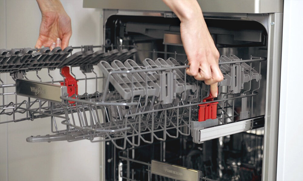 ZMYWARKA WHIRLPOOL WI9E 2B19 Na zdjęciu widoczne są dłonie unoszące i wysuwające górny kosz zmywarki, w którym zamocowano czerwone elementy regulacyjne. Ujęcie akcentuje system regulacji wysokości kosza, ułatwiający dopasowanie przestrzeni do wyższych naczyń i garnków regulacja górnego kosza 3,5 cm regulacji więcej miejsca duże naczynia elastyczna przestrzeń dopasowanie