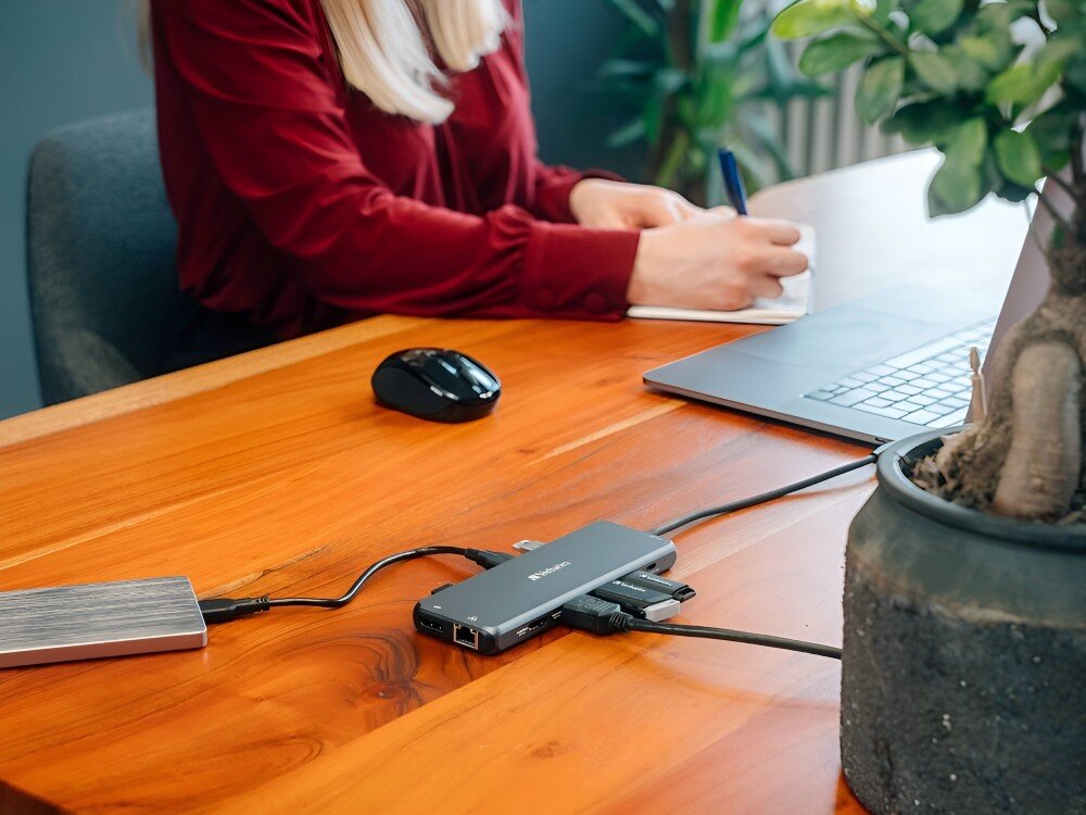 Hub Verbatim 32153 Hub leżący na drewnianym biurku podłączony do laptopa, z którego korzysta kobieta, na pierwszym planie roślina
hub obudowa aluminium wygląd kompaktowy lekki