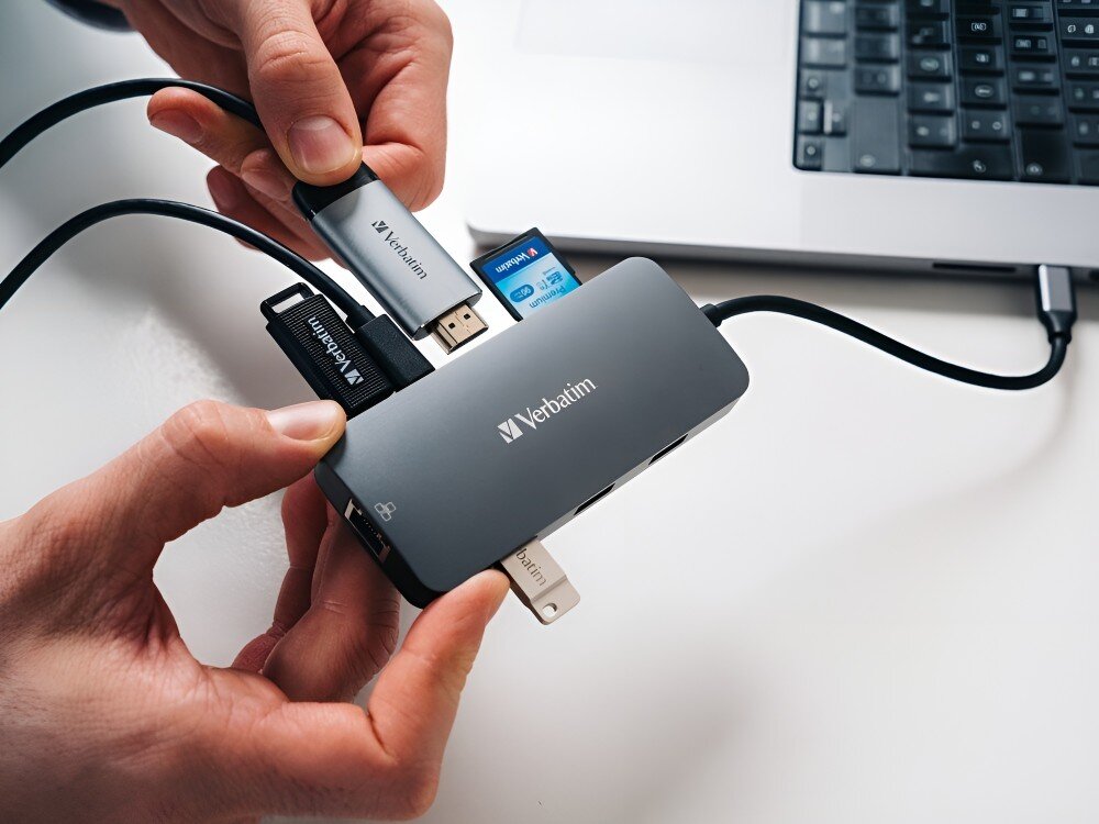 Hub Verbatim 32152 Ręce osoby podłączające różne nośniki danych do adaptera, w tym pendrive i kartę SD, obok otwartego laptopa,
            hub hdmi ethernet usb usbc sd microsd