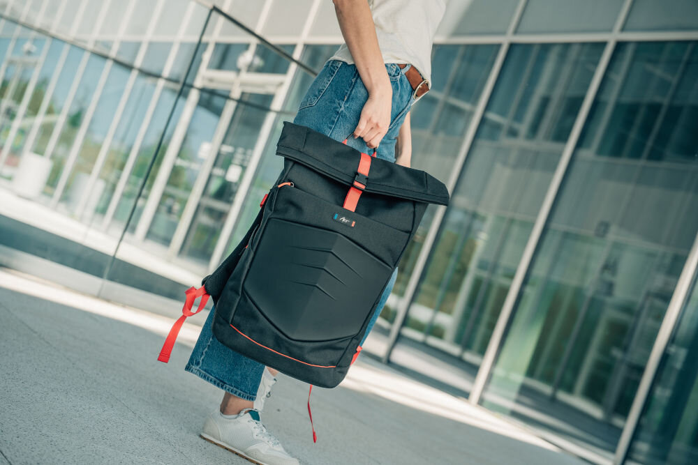 Plecak na laptopa ART BP-9367 15.6 cali prezentacja plecaka trzymanego za uchwyt przez kobietę w tle szklany budynek górny uchwyt transport wygodne noszenie w dłoni