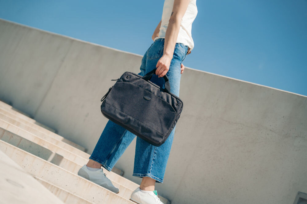 Torba na laptopa ART NB-0362 15.6 cali prezentacja torby trzymanej przez kobietę stojącej na schodach w tle betonowa ściana i bezchmurne niebo torba na laptopa do 15,6 cala