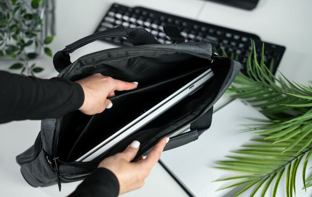 Torba na laptopa ART NB-0362 15.6 cali prezentacja otwartej torby trzymanej przez kobietę w środku laptop w tle białe biurko roślina klawiatura i otwarty notatnik smukła konstrukcja do transportu organizacja przestrzeni oszczędność miejsca
