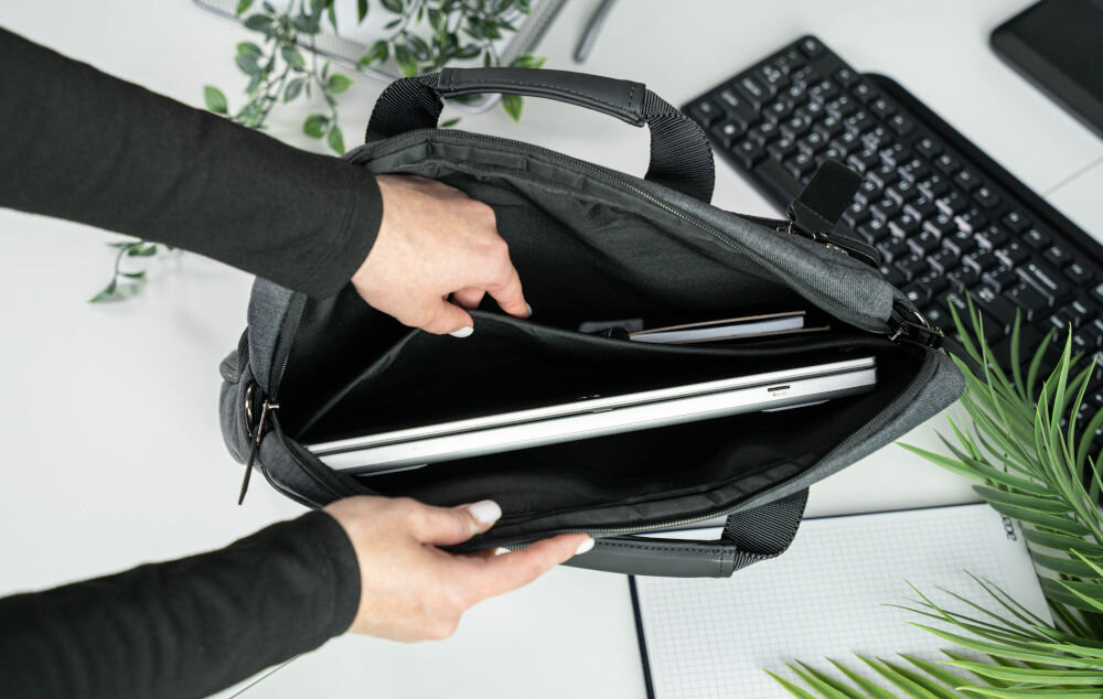 Torba na laptopa ART NB-0362 15.6 cali prezentacja otwartej torby trzymanej przez kobietę w środku laptop i notes w tle białe biurko klawiatura roślina torba do szkoły, pracy, biura estetyka funkcjonalność wygoda