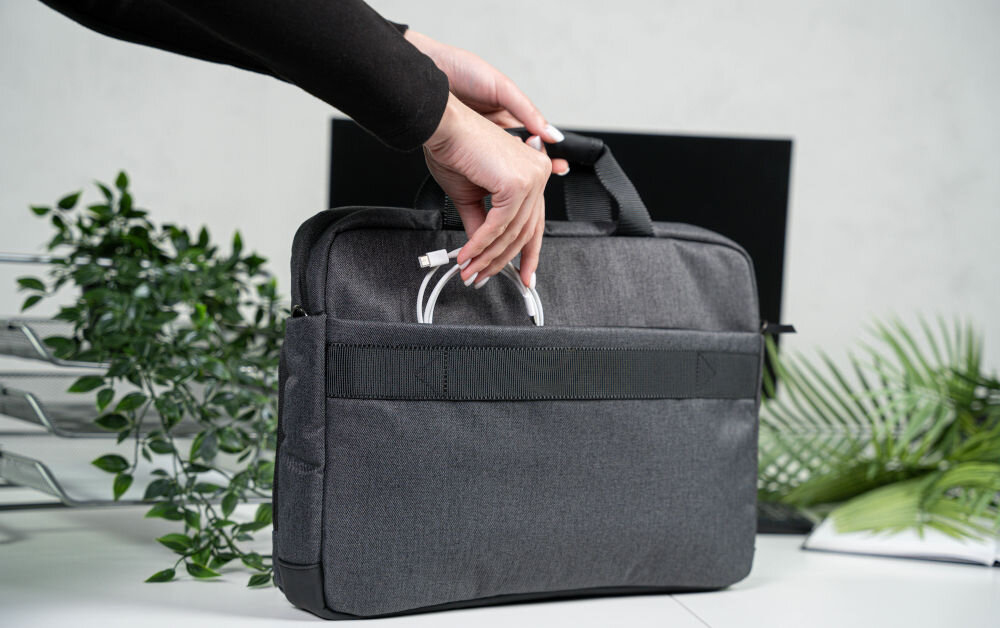 Torba na laptopa ART NB-0362 15.6 cali prezentacja torby od wewnętrznej strony trzymanej przez kobietę za uchwyt jedną ręką wkłada kabel do kieszeni w tle biurko rośliny monitor notes i stojak na dokumenty wymiary torby 40 × 29 × 6 cm codzienne użytkowanie ułatwia przechowywanie wygoda
