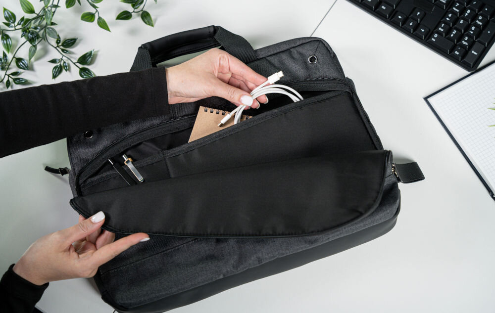 Torba na laptopa ART NB-0362 15.6 cali prezentacja otwartej przedniej komory torby w kieszeni kabel trzymany przez kobietę notes i długopisy w tle białe biurko otwarty notes klawiatura i roślina kieszeń na akcesoria z przodu funkcjonalność porządek