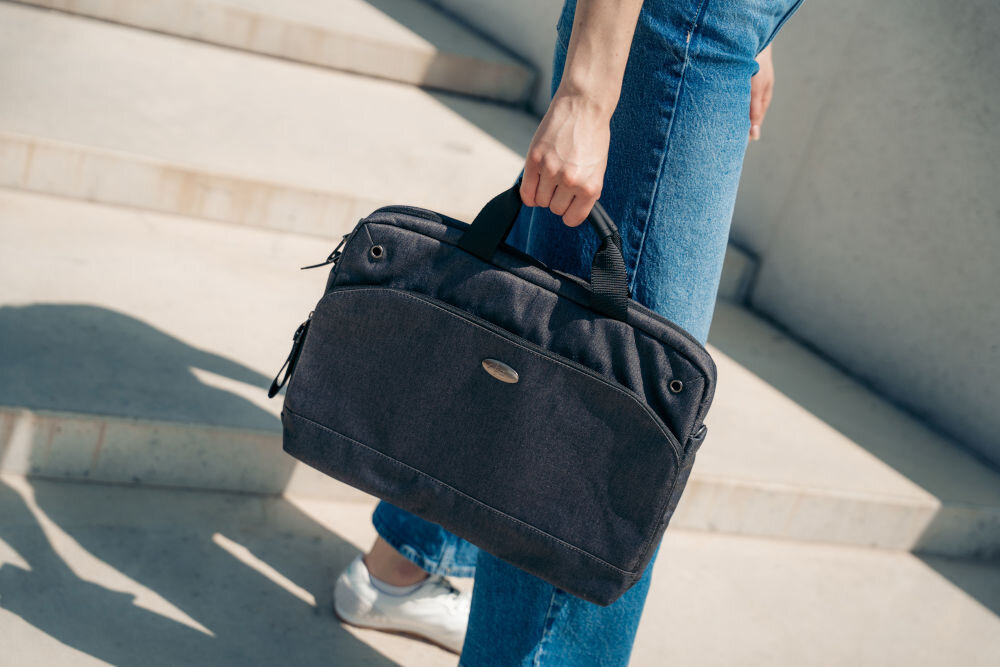 Torba na laptopa ART NB-0362 15.6 cali prezentacja torby trzymanej w ręce za uchwyt przez kobietę stojącej na schodach w tle betonowa ściana uchwyt do noszenia w dłoni wygoda szybki dostęp do zawartości