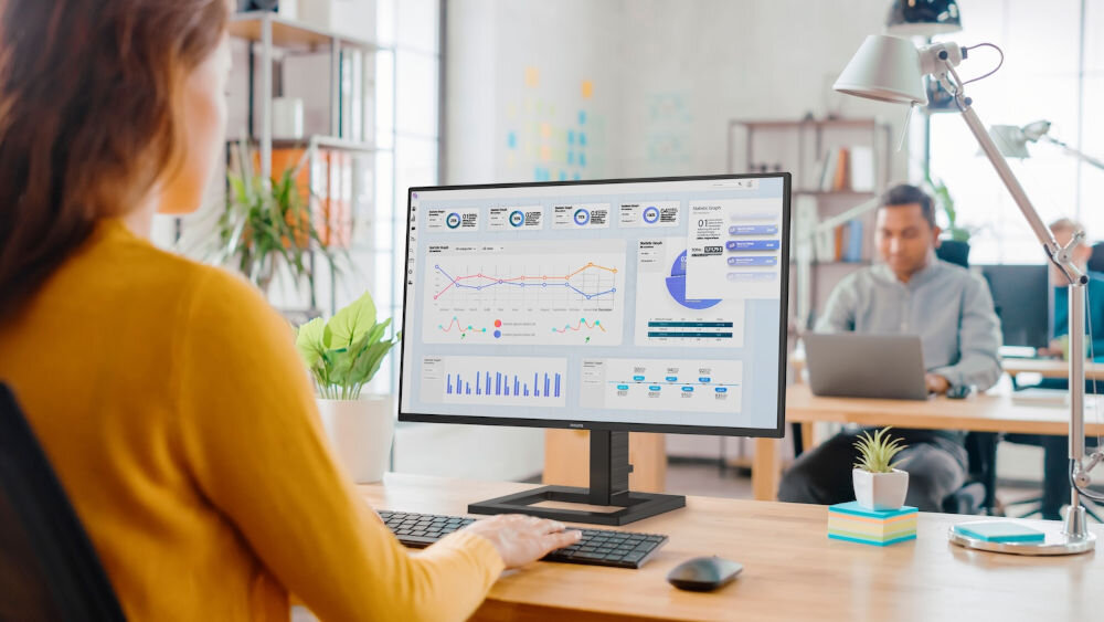 Monitor PHILIPS 27E1N1300AE 27 cali 1920x1080px IPS 100Hz 1 ms [MPRT] prezentacja monitora podczas użytkowania w biurze kobieta siedząca przed biurkiem
