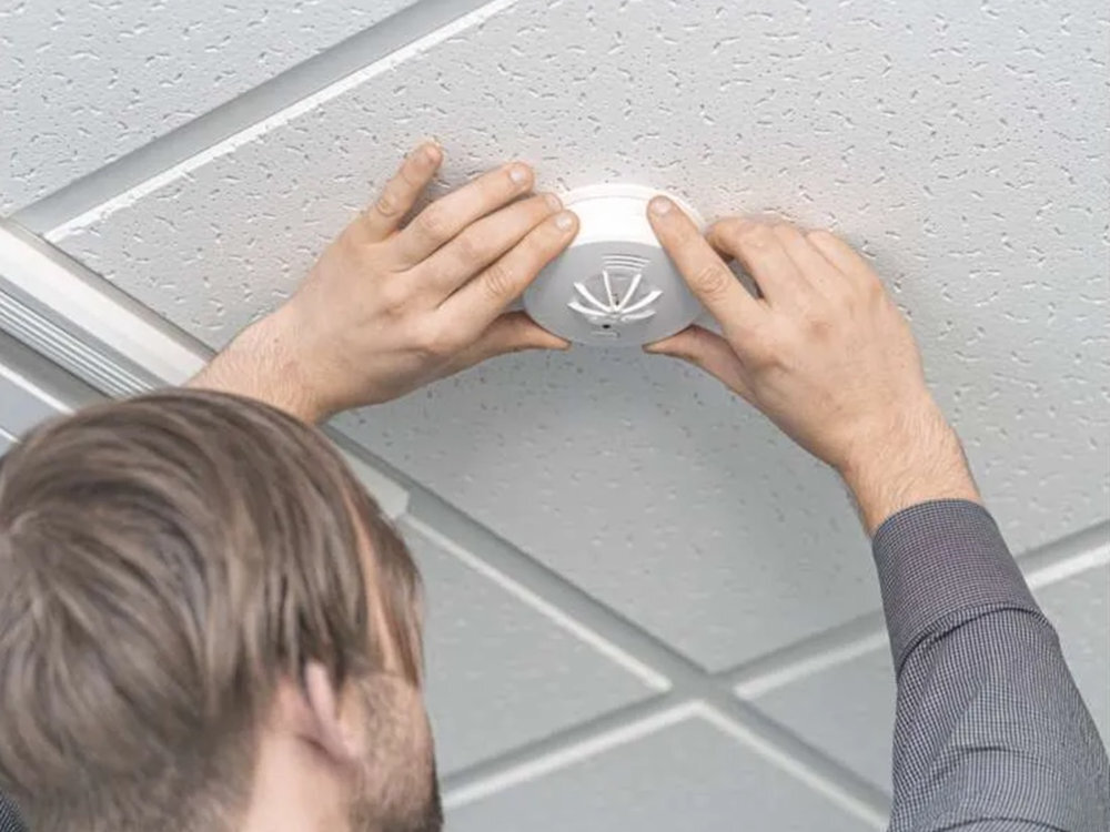 EMOS THS916A system, który uniemożliwia montaż bez baterii - czujniki umieszczone na suficie korytarza w hotelu szybko reaguje na zagrożenie - męzczyzna zawieszający czujnik na suficie