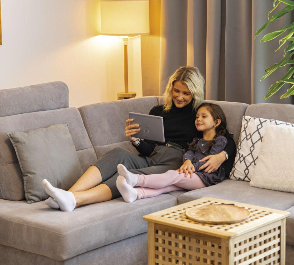 Wideodomofon EMOS GoSmart IP-09D H4030 Bezprzewodowy Wi-Fi, obraz, noc, IR, rozdzielczość, Kobieta z dzieckiem na sofie w salonie, razem oglądają tablet w przytulnym oświetleniu.