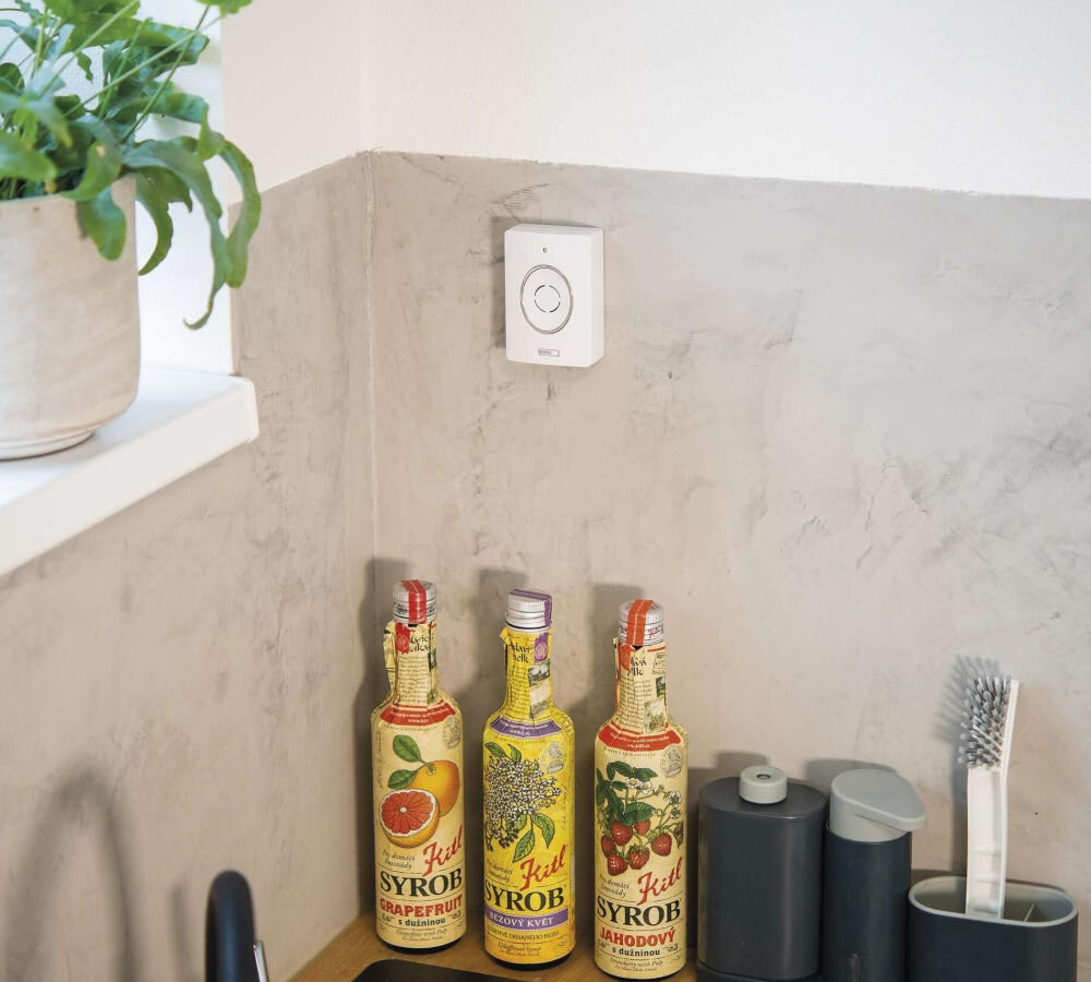 Wideodomofon EMOS GoSmart IP-09D H4030 Bezprzewodowy Wi-Fi, kompatybilność, Tuya, automatyzacja, scenariusze, Panel sterowania EMOS GoSmart na ścianie kuchni, obok trzy butelki syropów i akcesoria.