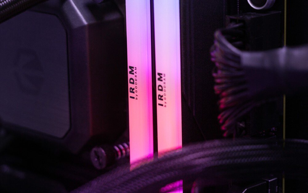 Pamięć RAM GOODRAM IRDM RGB Dwa moduły pamięci zamontowane w komputerze, emitujące różowo-fioletowe światło, otoczone przewodami i elementami chłodzenia