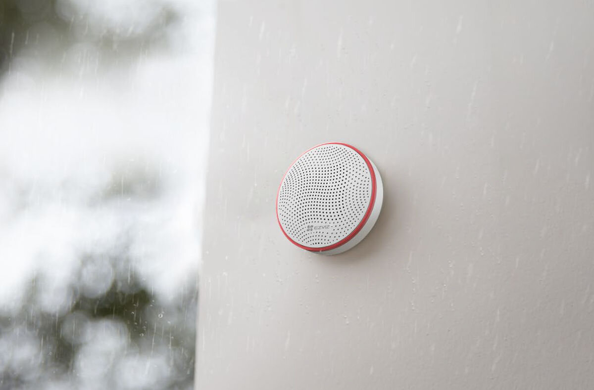 Syrena zewnętrzna EZVIZ CS-T9C-A0-BG, Szczelność IP54, praca zimą, odporność na deszcz, wysoka trwałość, Syrena alarmowa EZVIZ T9C zamontowana na ścianie zewnętrznej, widoczne krople deszczu