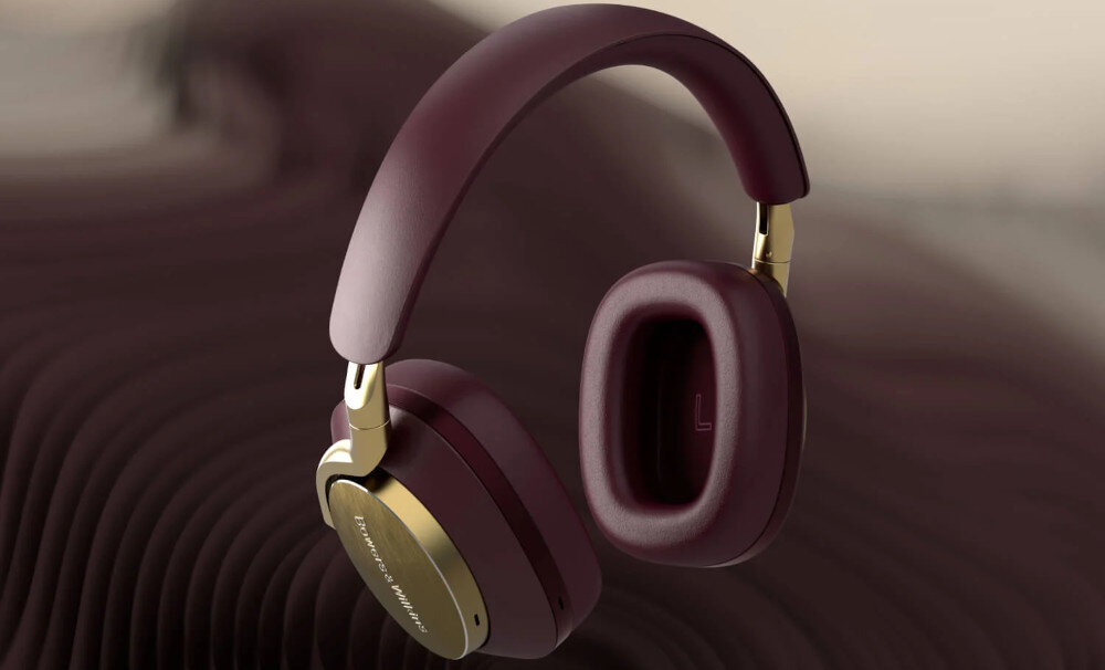 Bordowe słuchawki nauszne z metalicznymi elementami i widocznym logo \'BOWERS_WILKINS & Wilkins\' na nauszniku. Tło jest rozmyte w odcieniach brązu.