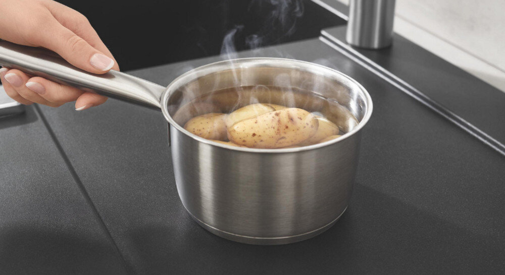 Zlewozmywak jednokomorowy GROHE K700 31650AP0 Na czarnym ociekaczu stoi gorący rondel z ziemniakami, trzymany za rączkę. Widoczna para pokazuje odporność powierzchni na wysoką temperaturę Wysoka odporność termiczna wysokie temperatury odporny gorące naczynia