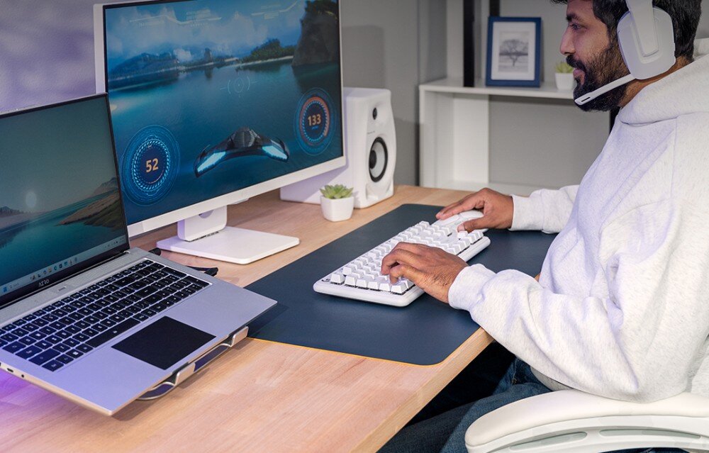 Pamięć RAM CRUCIAL Mężczyzna w słuchawkach grający na komputerze przy biurku z monitorem i białą klawiaturą