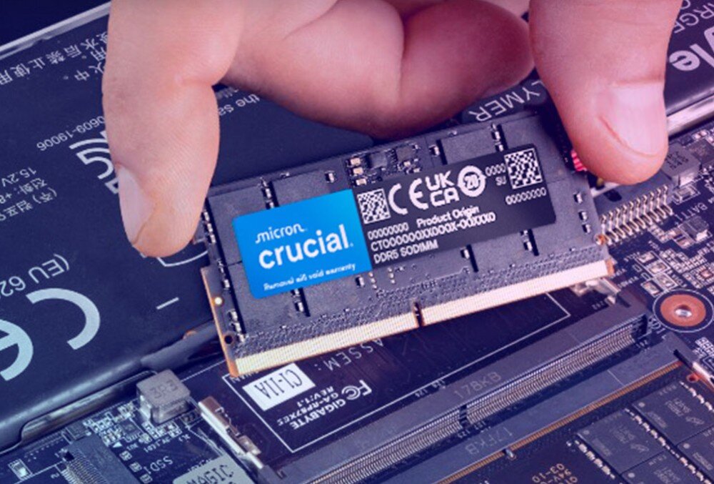 Pamięć RAM CRUCIAL Dłonie trzymające moduł pamięci RAM nad gniazdem wewnątrz otwartego laptopa