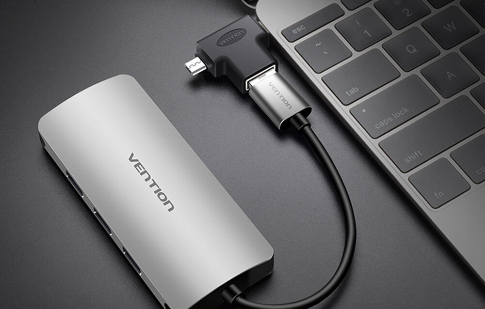 Na obrazie widoczny jest adapter z napisem \'vention\' podłączony do laptopa oraz srebrne urządzenie z kilkoma portami USB. Tło jest ciemne, a elementy mają metaliczne wykończenie.
