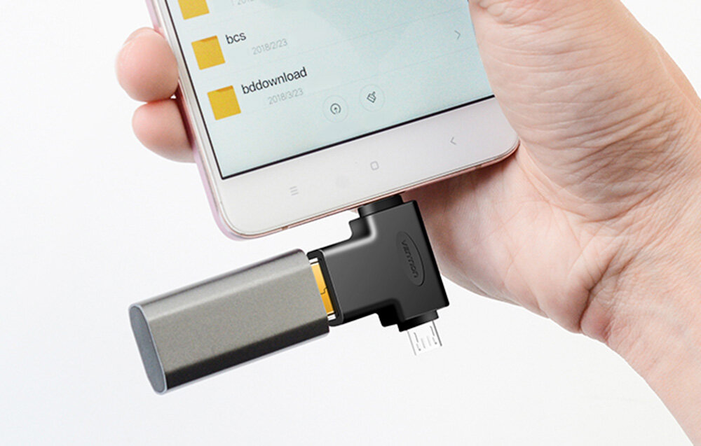 Osoba trzyma smartfon z podłączonym adapterem OTG, do którego wpięty jest pendrive. Na ekranie telefonu widoczne są foldery z datami: \'bcs\', \'bddownload\' z datą 2018/02/23.