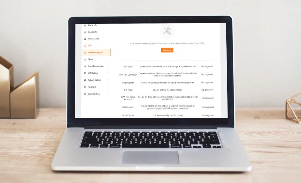 Router TENDA MX21 Pro Laptop stojący na drewnianym biurku z otwartym interfejsem diagnostycznym routera pokazującym zakładkę 'Network Diagnostic' z ikoną klucza i listą testów sieci