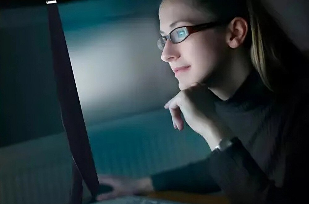 Monitor PHILIPS 49B2U6900CH Kobieta w okularach patrzy na ekran monitora w ciemnym otoczeniu. Jej twarz jest lekko oświetlona przez światło ekranu, ochrona wzroku