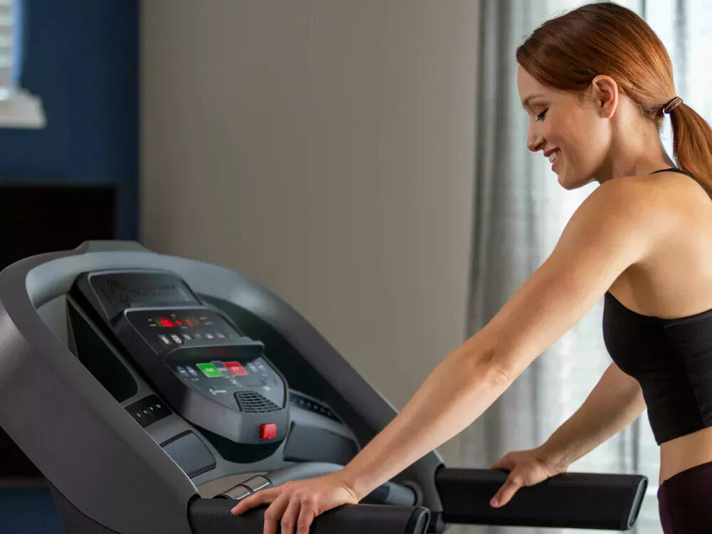 Bieżnia elektryczna HORIZON FITNESS T101 -27 1840W 18km-h pomieszczenie pokój osoba opiera dłonie na uchwytach w tle ściana i okno zintegrowane głośniki wejście audio in/out Bluetooth korzystanie z ulubionej muzyki lub aplikacji fitness funkcja audio daje opcję słuchania muzyki lub instrukcji treningowych ułatwia koncentrację i urozmaica sesję funkcje rozrywkowe wspierają utrzymanie regularnych ćwiczeń