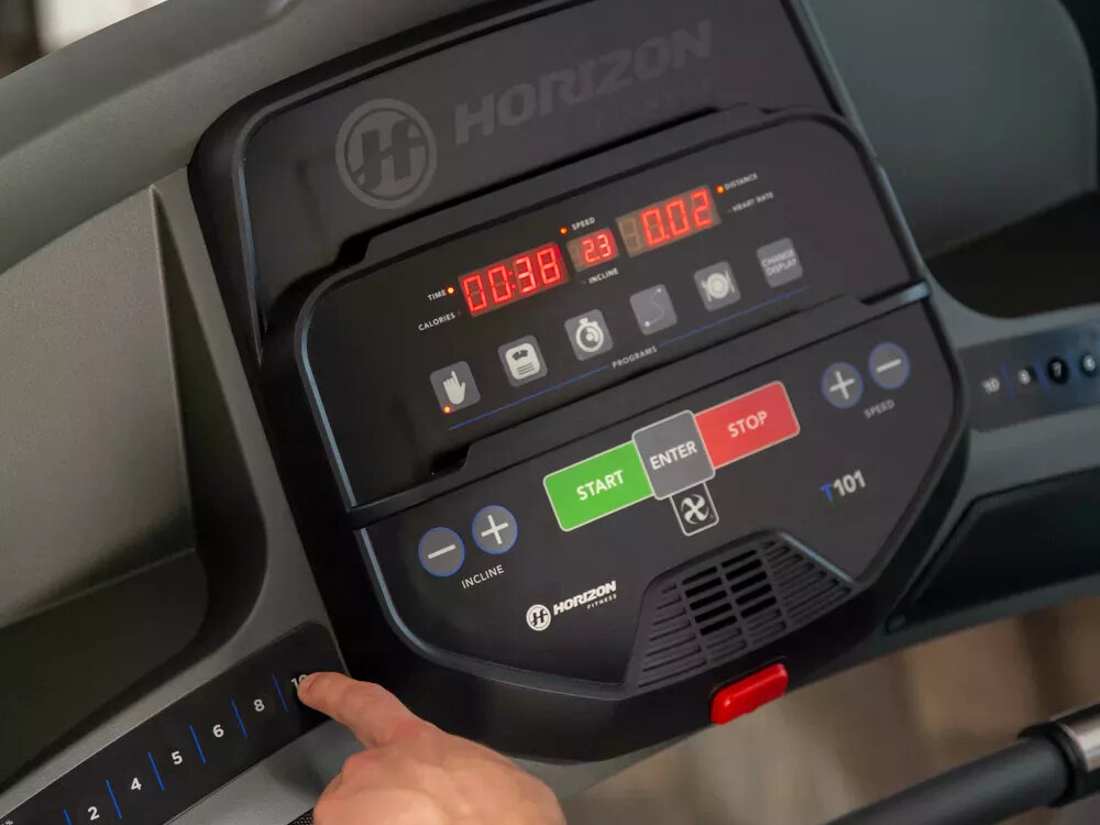 Bieżnia elektryczna HORIZON FITNESS T101 -27 1840W 18km-h zbliżenie na konsolę osoba trzyma palec na przycisku 35 programów treningowych ręczny interwałowy docelowy dystansu i spalania kalorii programy sterowane pulsem można dopasować trening do własnych potrzeb i celów