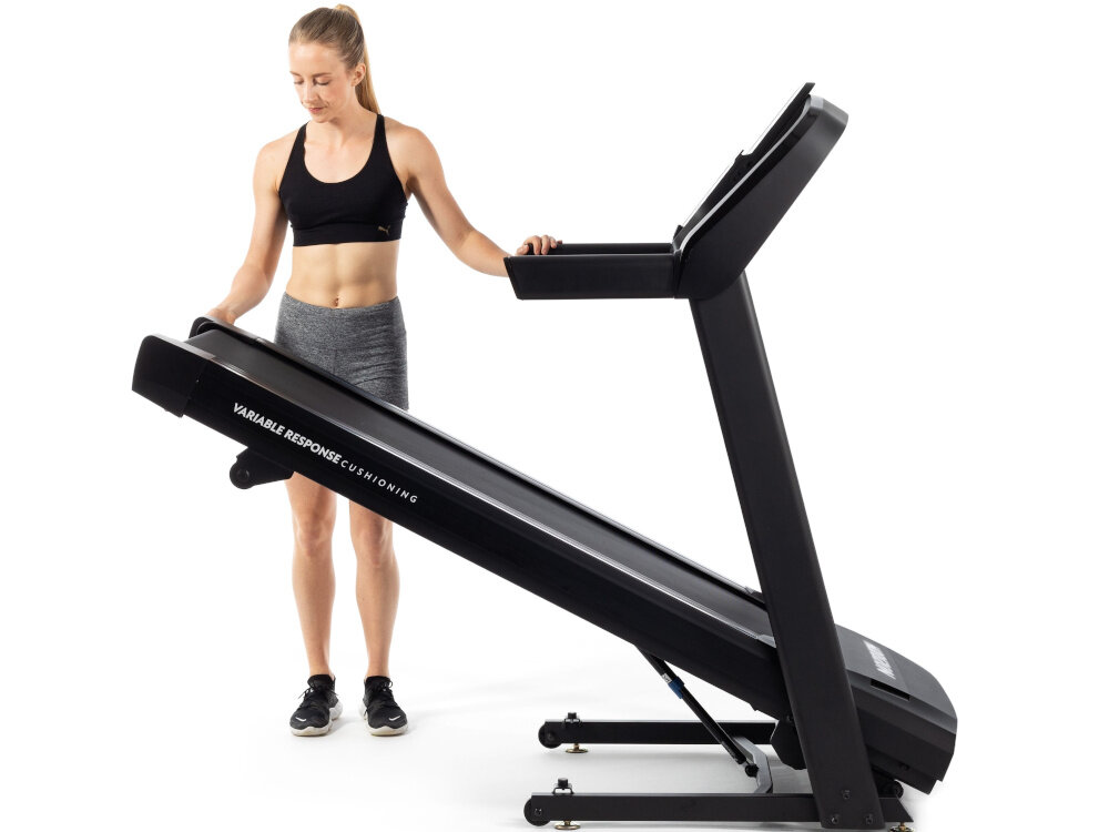 Bieżnia elektryczna HORIZON FITNESS T101 -27 1840W 18km-h bieżnia na białym tle osoba składa bieżnię mechanizm Feather Light Folding można łatwo złożyć bieżnię po treningu porządek w pomieszczeniu wymiary po złożeniu 116 x 70 x 144 cm