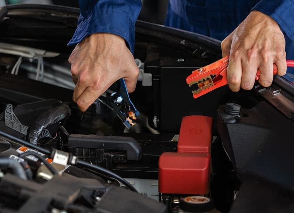 Przewody rozruchowe EXTRALINK EX.31931 warsztat samochód silnik osoba trzyma klamry przewodów w dłoniach podłącza je do akumulatora pewny rozruch bezpieczeństwo wszechstronność