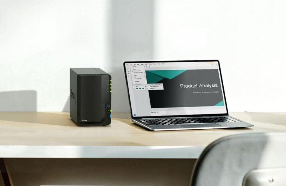 Serwer plików SYNOLOGY DiskStation DS224+ Na zdjęciu widoczny jest laptop na jasnym biurku z uruchomioną aplikacją do analizy produktu. Po lewej stronie laptopa stoi niewielki, czarny serwer plików, przeznaczenie, podzespoły, działanie, dyski
