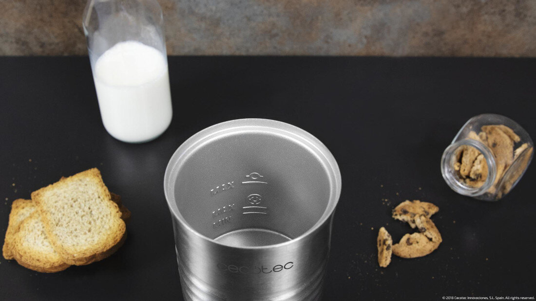 Na stole znajduje się metalowy pojemnik z logo \'cecotec\', obok którego leży kilka kromek chleba i rozsypane ciastka. W tle widoczna jest butelka z mlekiem.