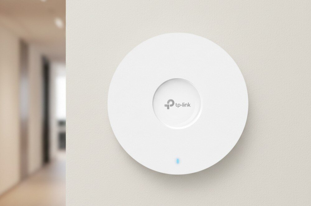 Punkt dostępu TP-LINK EAP670 Okrągły punkt dostępowy z logo tp-link na środku i diodą w dolnej części zamontowany na płaskiej powierzchni
