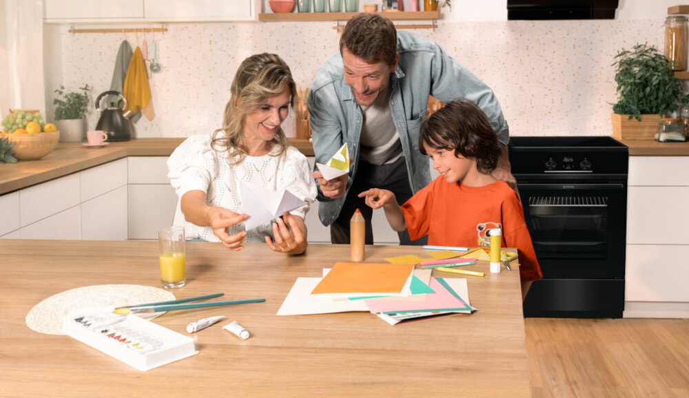KUCHNIA GORENJE MEKIS510IB lifestyle kuchnia rodzina dziecko akcesoria plastyczne na stole kuchenka w tle kolor czarno srebrny okap półki czajnik akcesoria kuchenne na blacie