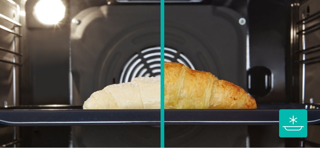 KUCHNIA GORENJE MEKIS510IB Wnętrze piekarnika pokazane w przekroju z jedną rogalikową bułką na blasze, po lewej stronie widoczny jest surowy jasny rogalik, a po prawej ten sam wypiek już zarumieniony i upieczony, co ilustruje efekt delikatnego podgrzewania lub rozmrażania FrozenBake do mrożonek