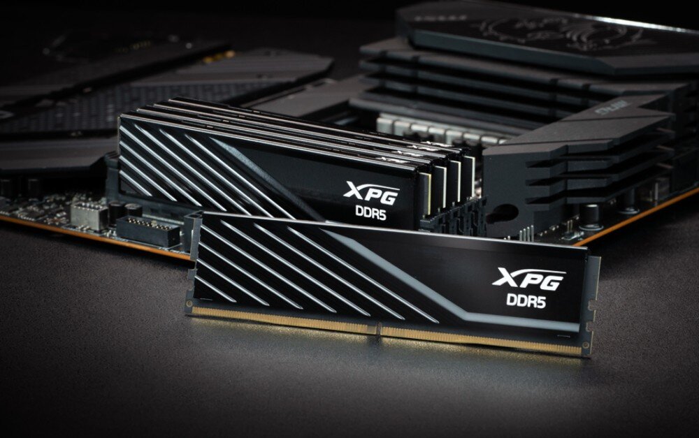 Pamięć RAM ADATA XPG Lancer Blade Zbliżenie na czarny moduł pamięci zainstalowany w gnieździe płyty głównej bezpośrednio pod aluminiowymi żeberkami chłodzenia procesora, widoczne jest logo i napis 'DDR5' na boku obudowy, radiator, wielkość