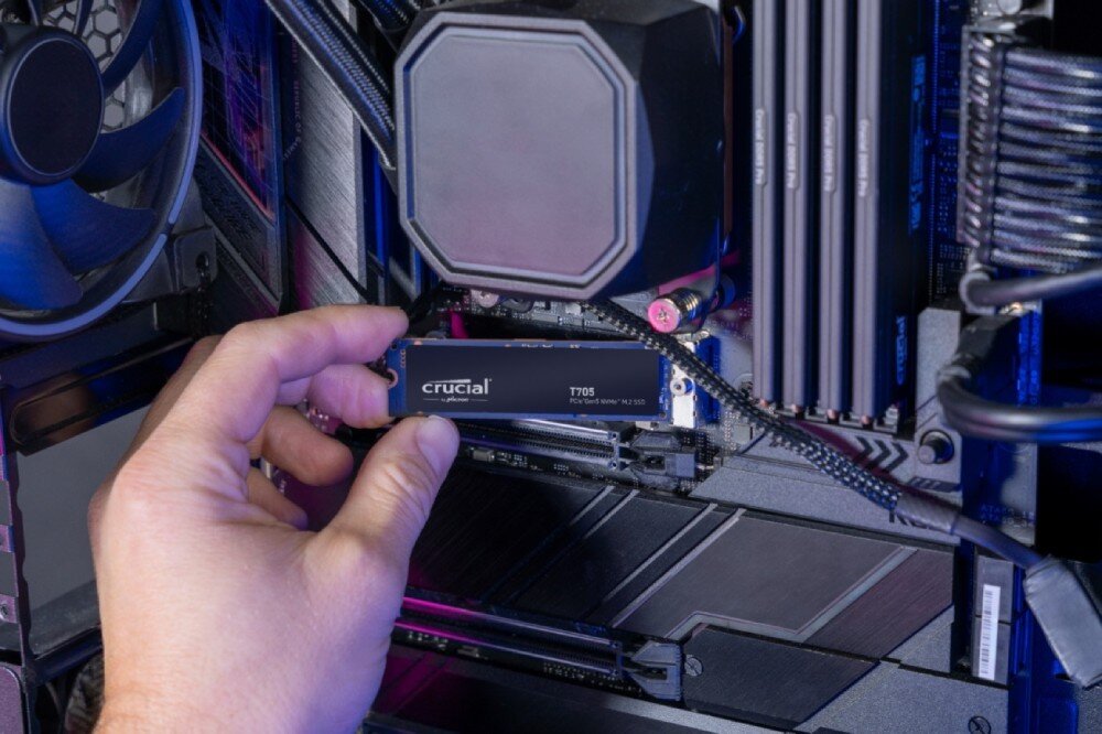Dysk CRUCIAL T705 Montaż dysku SSD 'T705' wewnątrz obudowy komputera przez osobę trzymającą go palcami, widoczne wentylator, moduły RAM i chłodzenie procesora, interfejs, funkcje, technologia