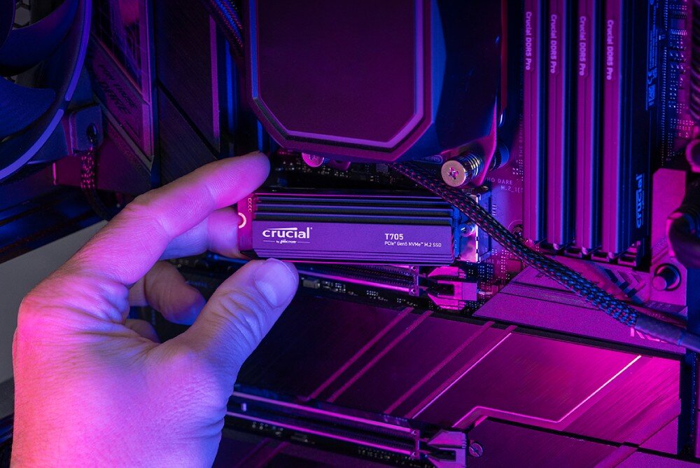 Dysk CRUCIAL T705 Ręka trzymająca czarny dysk SSD przy instalacji w komputerze, widoczne podzespoły i fioletowo-niebieskie światło, interfejs, funkcje, technologia