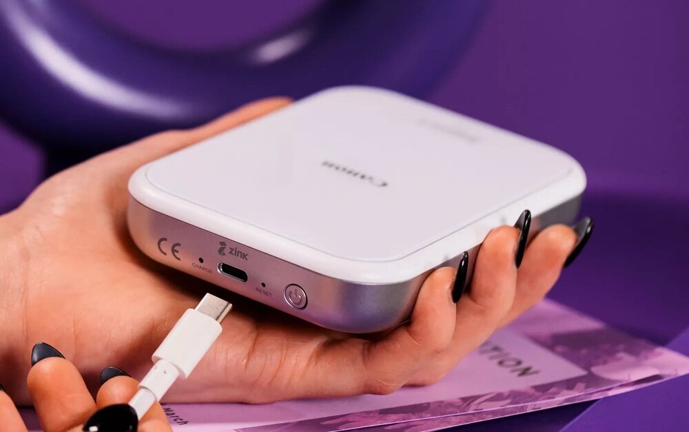 Osoba trzyma różowo-białą drukarkę z logo \'Canon\' na górze. Na urządzeniu widoczne są oznaczenia CE, Zink oraz port USB-C.