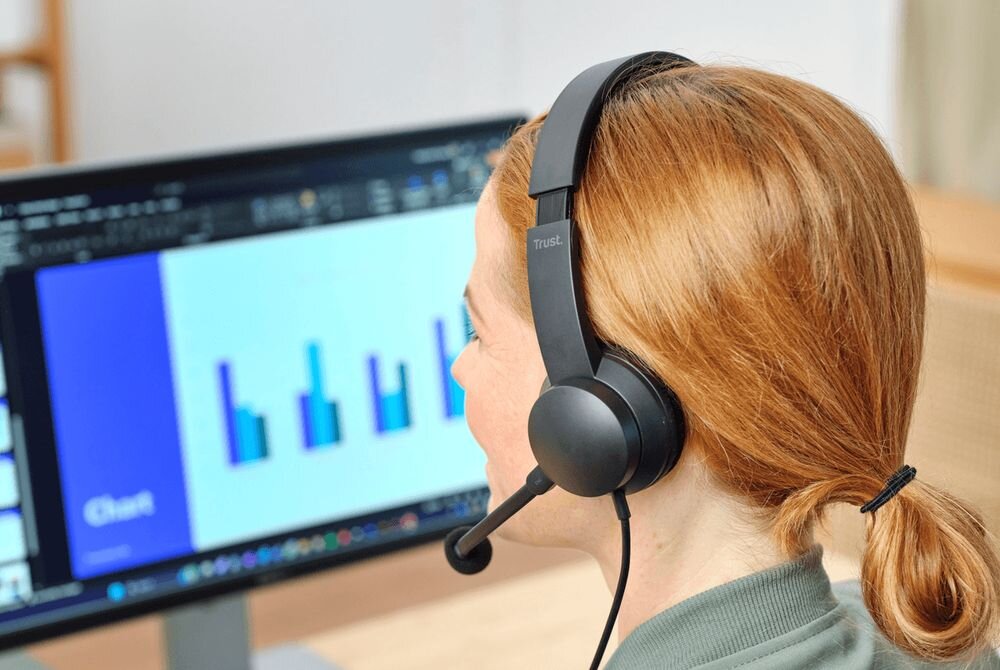 Słuchawki TRUST Ayda USB-C zestaw słuchawkowy do pracy i rozmów online, osoba z założonymi słuchawkami pracująca przy komputerze