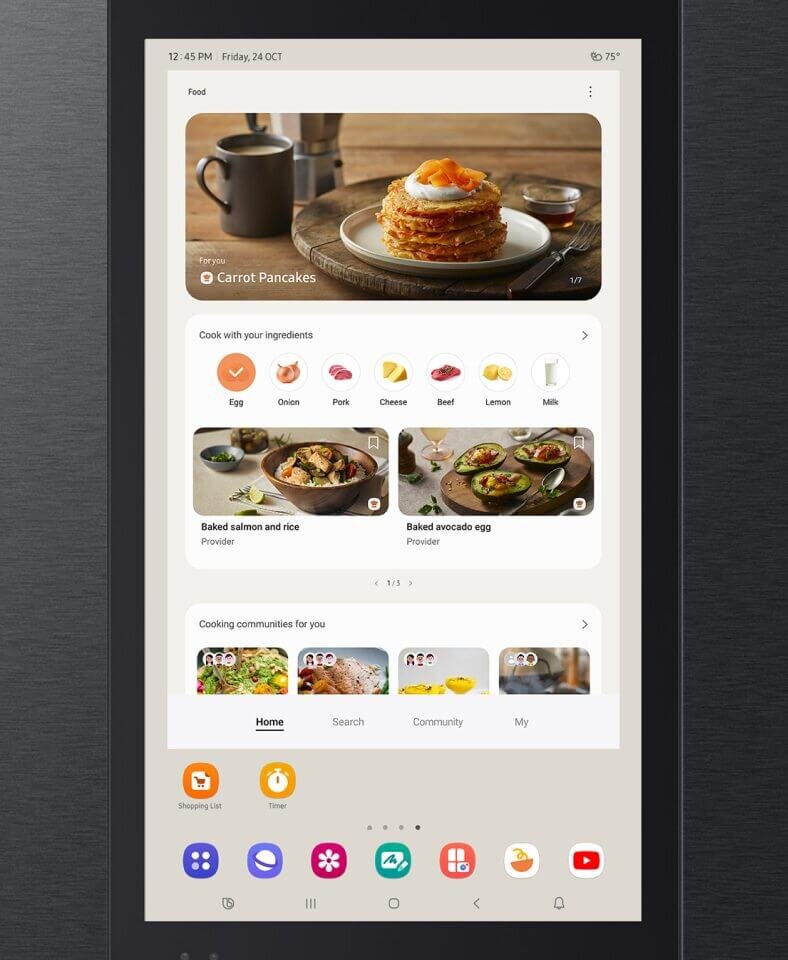 Ekran urządzenia wyświetla aplikację z przepisami kulinarnymi, z widocznym zdjęciem naleśników z marchewką oraz listą składników do wyboru. Na dole ekranu znajdują się ikony aplikacji, takie jak lista zakupów i timer.