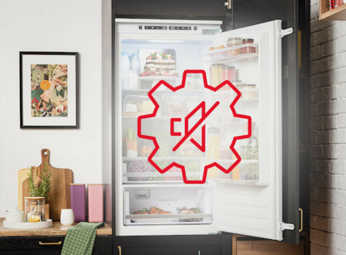 Otwarta lodówka z widocznymi półkami pełnymi jedzenia, na drzwiach znajduje się czerwony symbol przekreślonego mikrofonu w kształcie zębatki. W tle widoczna jest kuchnia z obrazem na ścianie i akcesoriami kuchennymi na blacie.