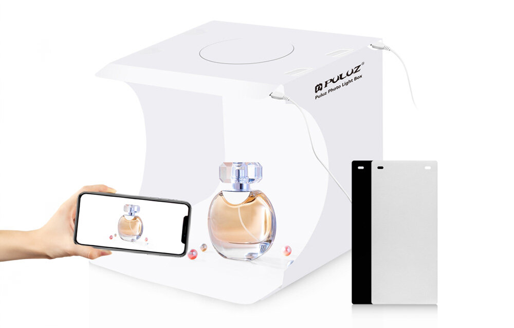 Na obrazie widoczny jest namiot bezcieniowy z logo \'Puluz Photo Light Box\', w którym znajduje się flakon perfum. Obok namiotu znajduje się ręka trzymająca smartfon z wyświetlonym zdjęciem flakonu oraz dwie prostokątne plansze w kolorach białym i czarnym.
