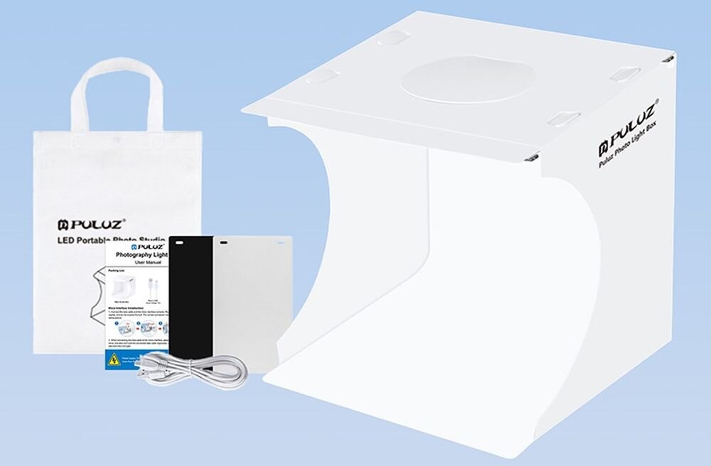 Na obrazie znajduje się biały namiot bezcieniowy z logo \'PULUZ Photo Light Box\'. Obok widoczna jest biała torba z napisem \'PULUZ LED Portable Photo Studio\', dwa tła w kolorze czarnym i białym, kabel oraz instrukcja obsługi.