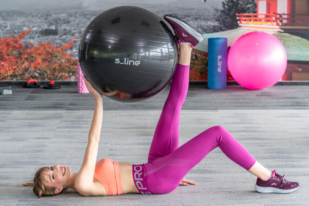 Piłka gimnastyczna S_LINE SA009N Czarny (65 cm) osoba ćwicząca z piłką podnoszenie piłki obciążenie do 180 kg