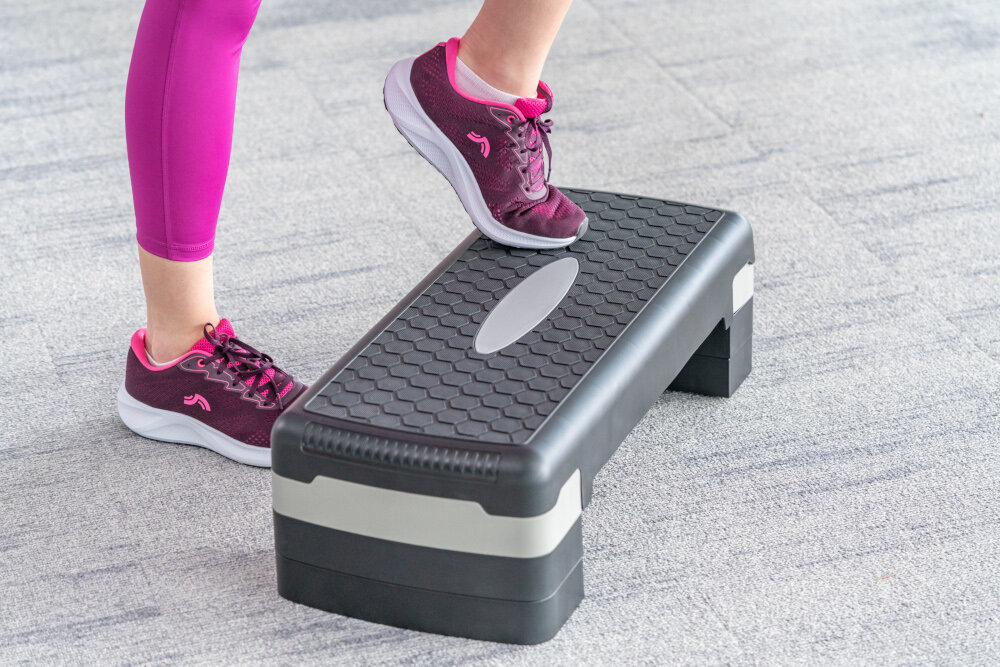 Step S_LINE SA022BG Czarno-szary sala gimnastyczna osoba ćwiczy na stepie jedna zbliżenie na stopy powierzchnia 81 × 28 cm antypoślizgowa struktura platformy pewność ruchu