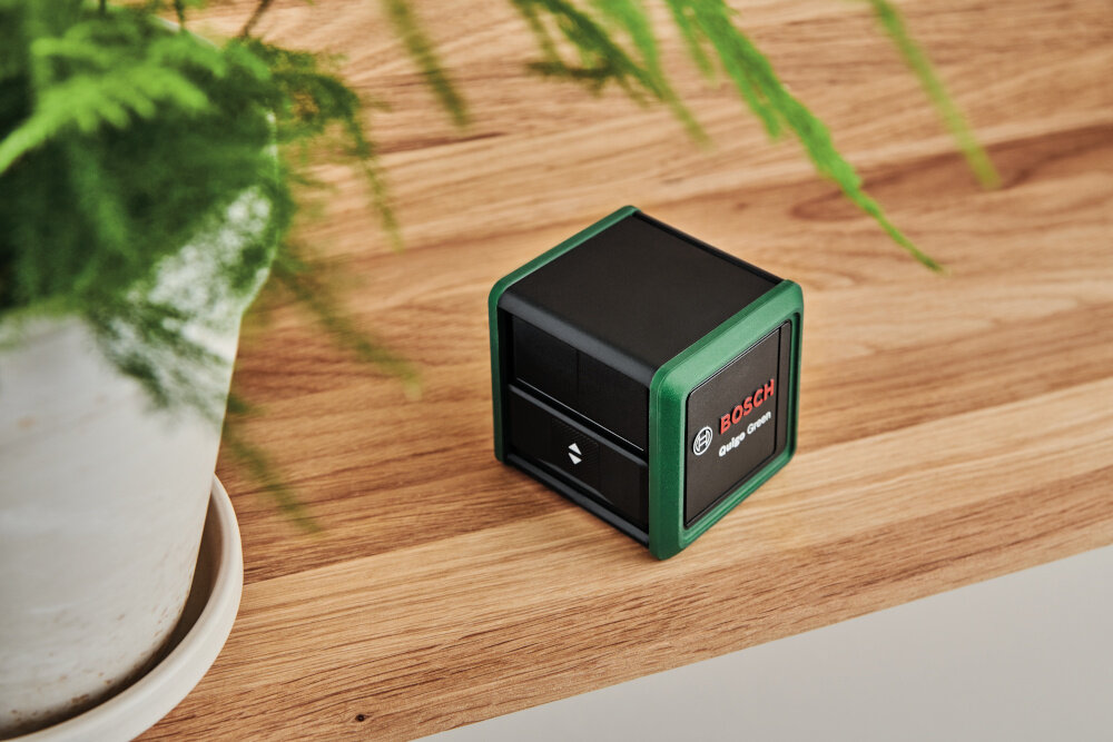 Laser krzyżowy BOSCH Quigo Green Set 0603663CZ1 pomieszczenie drewniany stolik na stoliku laser i kwiat widok z góry uniwersalne zastosowanie dokładność pomiarów