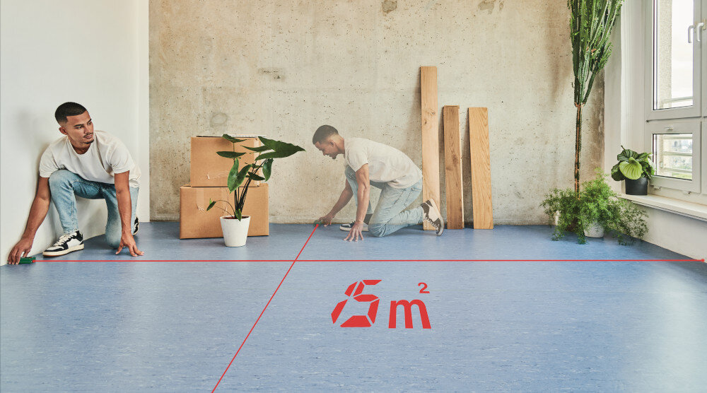 Dalmierz laserowy BOSCH EasyDistance 20 0603672AZ0 20m pomieszczenie pokój osoba mierzy powierzchnię podłogi widoczne dwie czerwone wiązki lasera wartość 15 m2 planowanie zakupów materiałów unikanie strat skrócenie czasu realizacji projektów efektywność prac remontowych montażowych czy dekoracyjnych