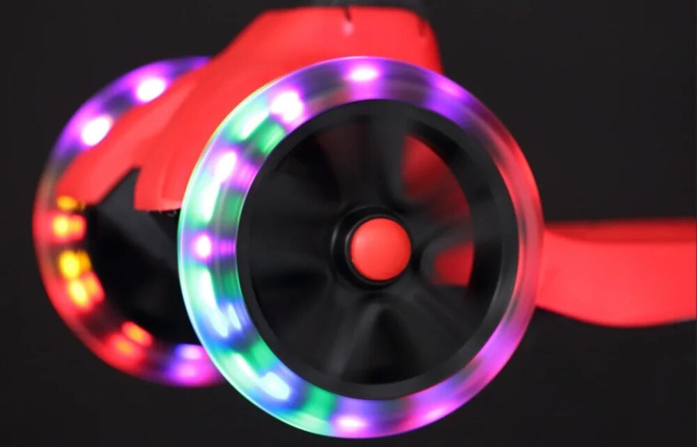 Hulajnoga dla dzieci EXTRALINK Dumbo Cruiser Czerwono-czarny ciemne tło zbliżenie na przednie kółka dwa przednie, świecące kółka przyciągają uwagę zwiększają widoczność dziecka efekt świetlny uruchamia się wraz z obrotem kół bez użycia baterii