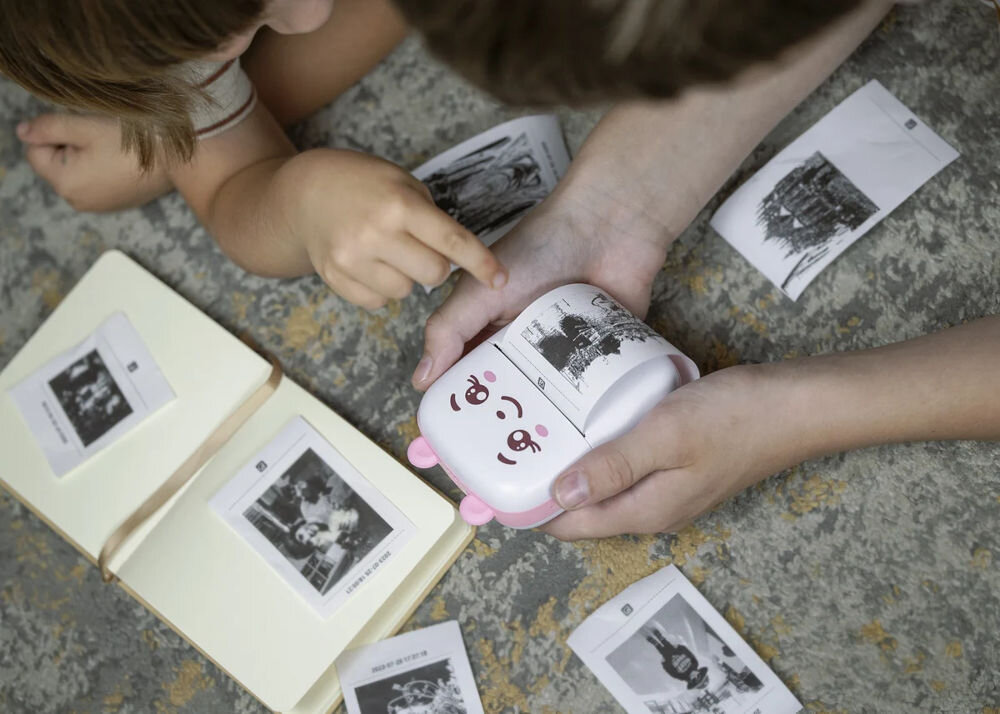 Drukarka EXTRALINK EPP-002 Złącze USB Niebieski + Papier termiczny samoprzylepny (5 szt.) drukarka trzymana w dłoniach drukująca zdjęcie w tle porozrzucane zdjęcia z telefon osoba siedząca z dzieckiem torba plecak przeniesienie zdjęć i notatek z telefonu na papier Bluetooth Android iOS